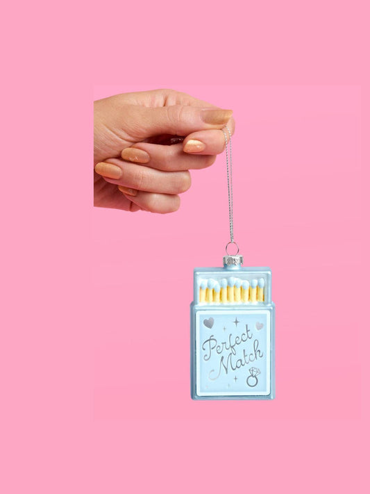 Hand holding blue matchbox engagement ornament by attached silver hanging string
