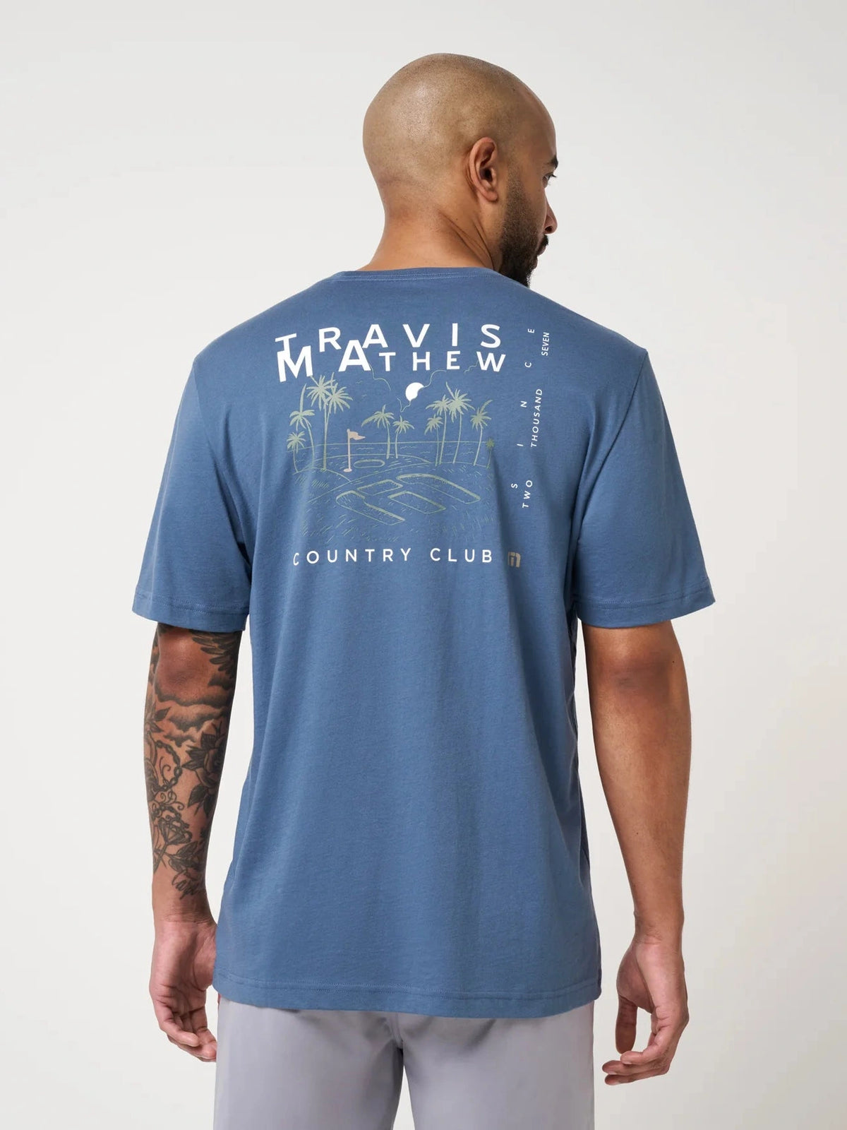 Back view of men's blue golf t-shirt featuring large palm tree and flag graphic
