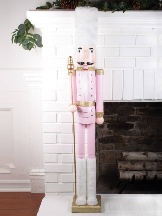 4ft pink holiday nutcracker standing on gold glitter base by fireplace